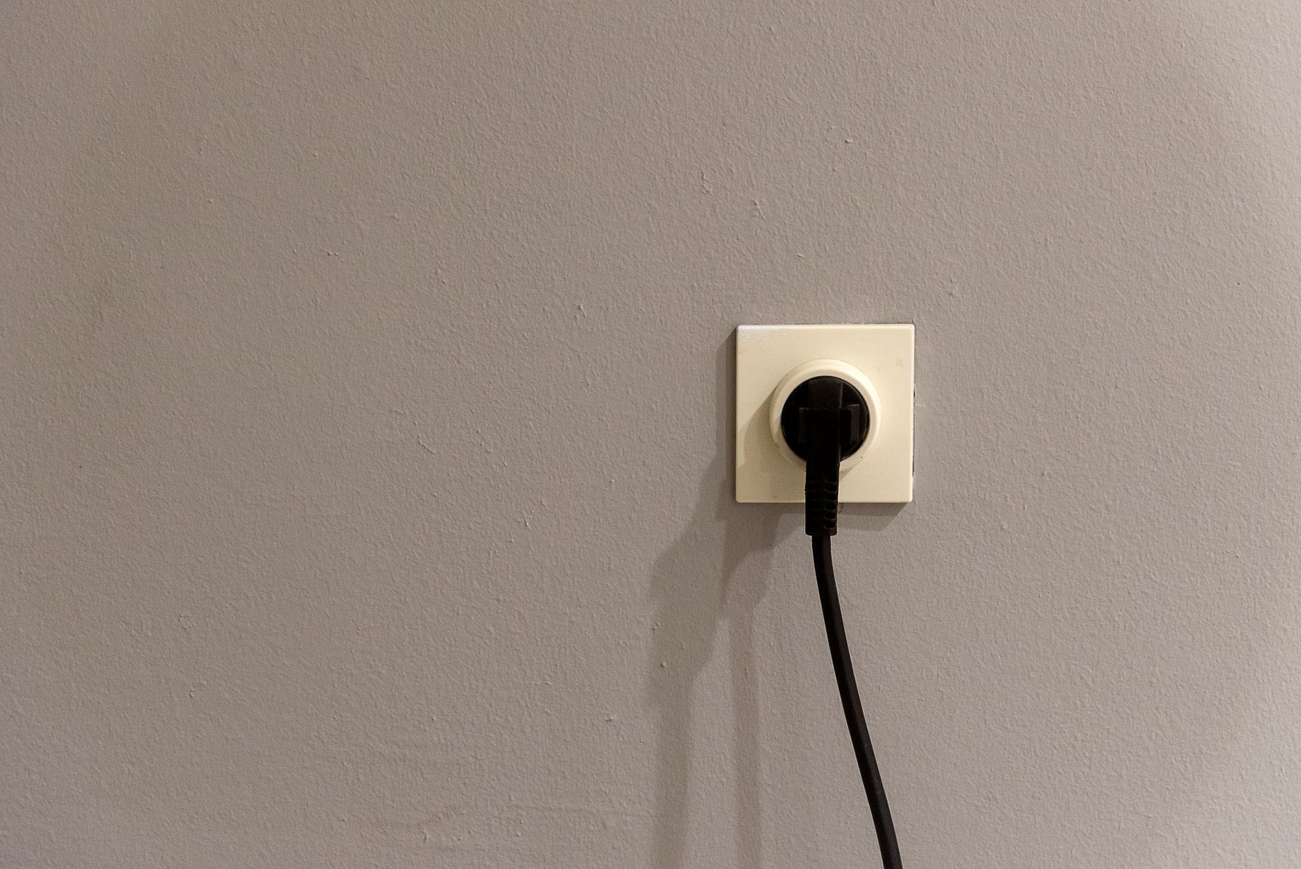 Gniazdka elektryczne w domu z dziećmi: co zabezpieczyć w pierwszej kolejności Czarna wtyczka podłączona do białego gniazdka w szarej ścianie